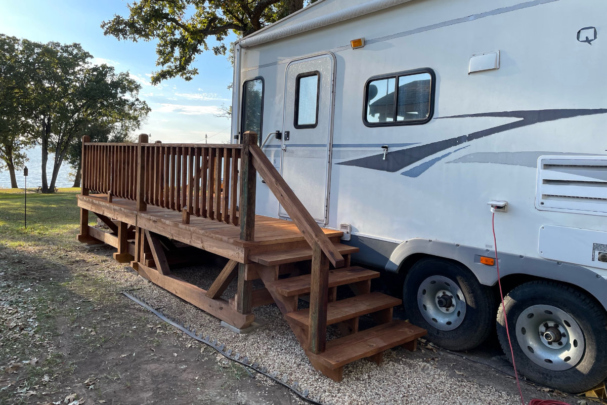 Dark-stained portable deck with stairs beside an RV